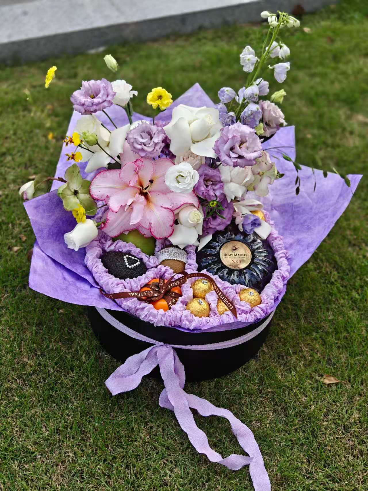 Bouquet of flowers with fruits wrapped in purple paper on a grassy background